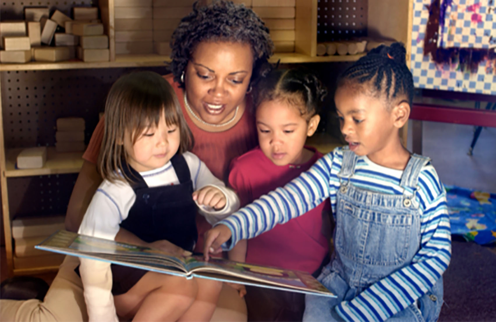 Preschool Teacher surrounded by students reading a book
