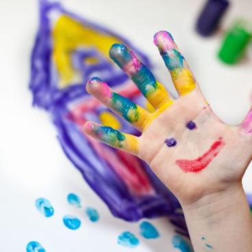 Child hand in finger paint with a smiley face in their palm